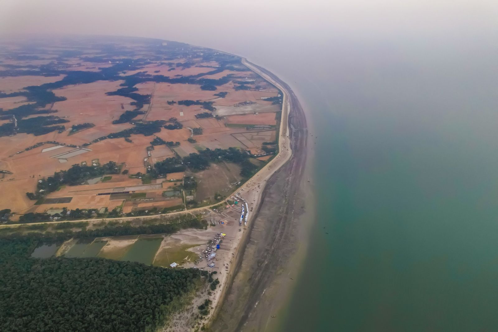 Aerial view of a coastline with an embankment, farmland and mangrove forest