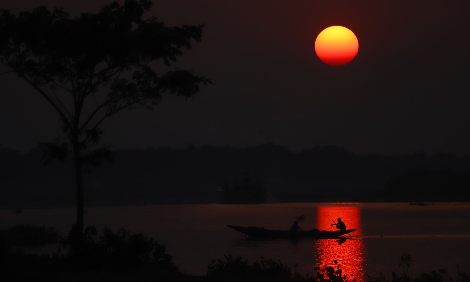 A boat on a river at sunset, in silhouette